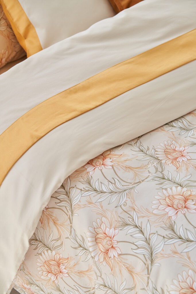 Dekbedovertrek op bed in katoen satijn met bloemenmotief in zacht geel en beige
